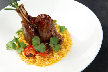 Risotto yastığında kuzu şişi, siyah bir arka planda bir tabakta.