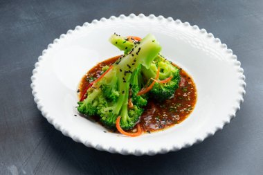 Gri arka planda, tabakta sos ile pişirilmiş brokoli. Seçici odak.