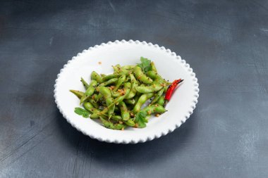 Gri arka planda bir tabakta baharat bulunan kızarmış baklagil kapsülleri. Seçici odak.