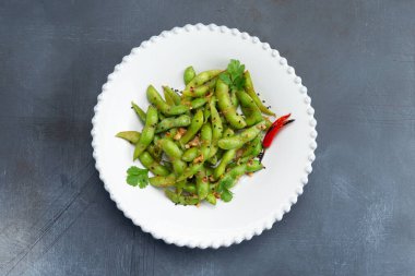 Gri arka planda bir tabakta baharat bulunan kızarmış baklagil kapsülleri. Seçici odak.