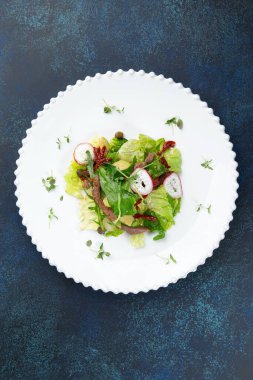 Etli salata, güneşte kurutulmuş domates ve bir tabakta turp. Karanlık bir arka plana karşı. Seçici odak.