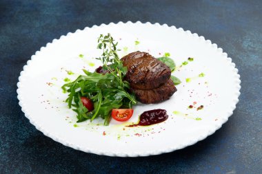 Roka ve domatesli biftek madalyonları. Karanlık bir arka plana karşı. Seçici odak.