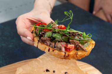 Elleri et, domates ve bitkilerle dolu bir bruschetta tutuyor. Karanlık bir arka plana karşı. Seçici odak.