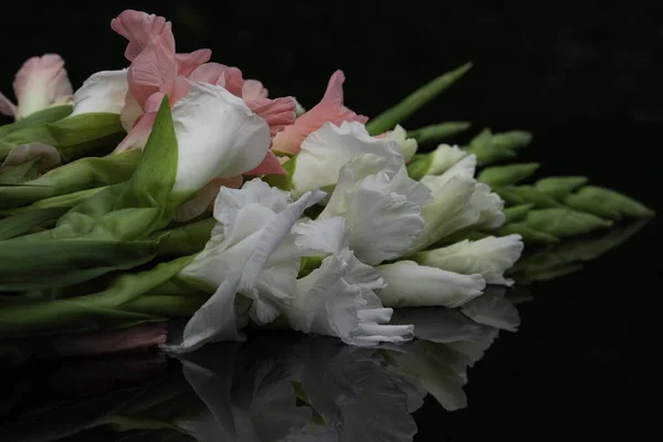 Bir buket gladioli, ıslak, siyah bir masanın üstünde.