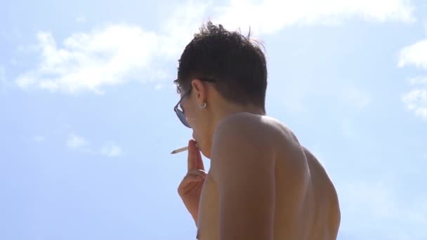 ビーチでメガネの若い男性は、タバコを吸う — ストック動画