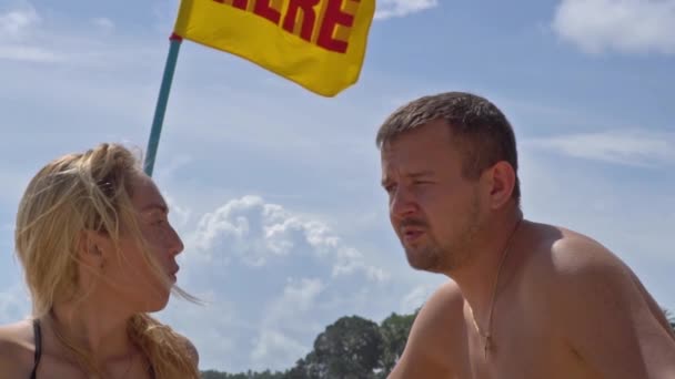 Ein Paar, das sich streitet. Strand auf dem Hintergrund einer Flagge mit der Aufschrift - hier — Stockvideo