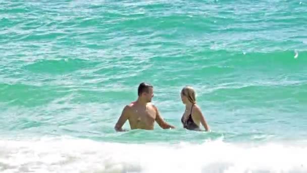Закохана пара на пляжі, що плаває в штормовому океані — стокове відео