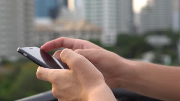 Homme naviguant sur le réseau social en utilisant le téléphone mobile à l'heure du soir au toit dans la grande ville. Gros plan. 4k — Video