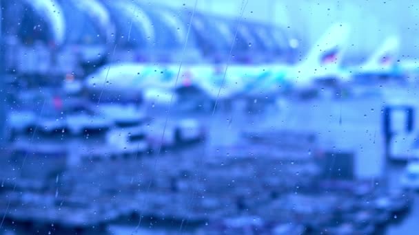 Gotas de lluvia en la ventana de la terminal del aeropuerto con el aeropuerto borroso fuera — Vídeo de stock