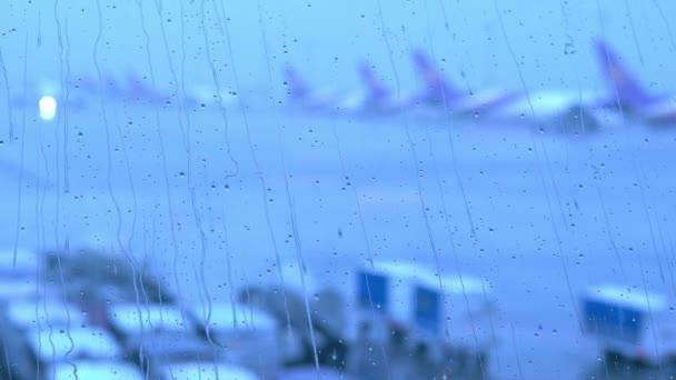 Gotas de lluvia en la ventana de la terminal del aeropuerto con el aeropuerto borroso fuera — Vídeo de stock