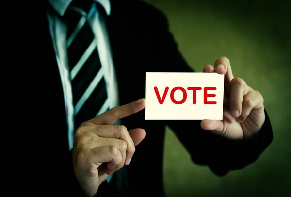Businessman showing vote card in hand with a dark background.