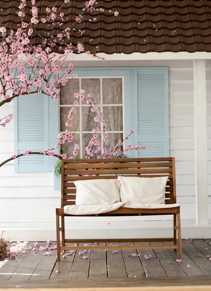 brown wooden bench with pillow near the cherry blossoms