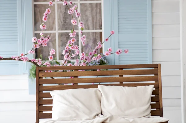 brown wooden bench with pillow near the cherry blossoms