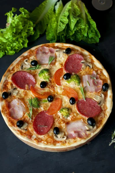 Pizza with salami, bacon, broccoli, olives on dard background. — Stock Photo, Image