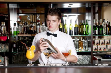Young handsome barman standing in front of the bar clipart