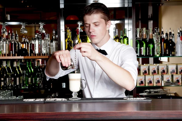Jovem barista bonito fazendo latte atrás do bar no café . — Fotografia de Stock