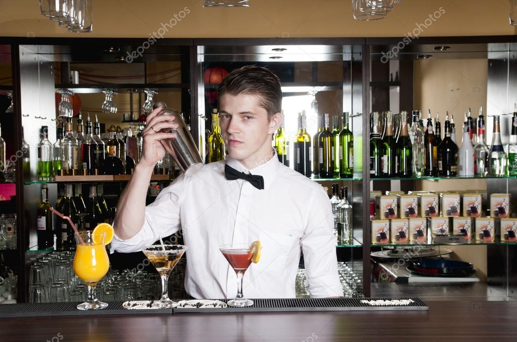 Young handsome barman standing in front of the bar