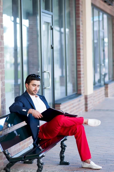 Jeune homme élégant reposant sur un banc, lisant un magazine . — Photo