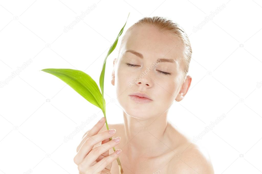 Woman with a healthy and well-groomed complexion holding green leaf in front of her face.
