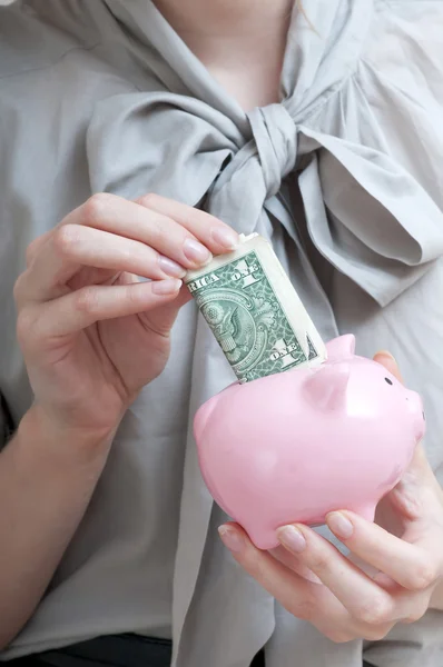 Mão feminina colocando um dólar em um banco porquinho . — Fotografia de Stock