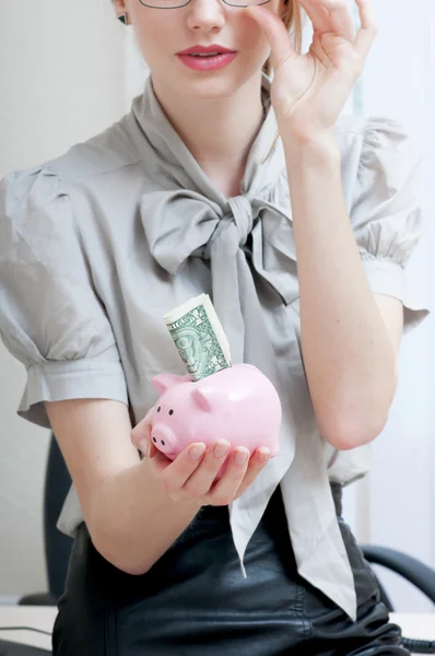 Mão feminina segurando banco porquinho contendo um dólar . — Fotografia de Stock