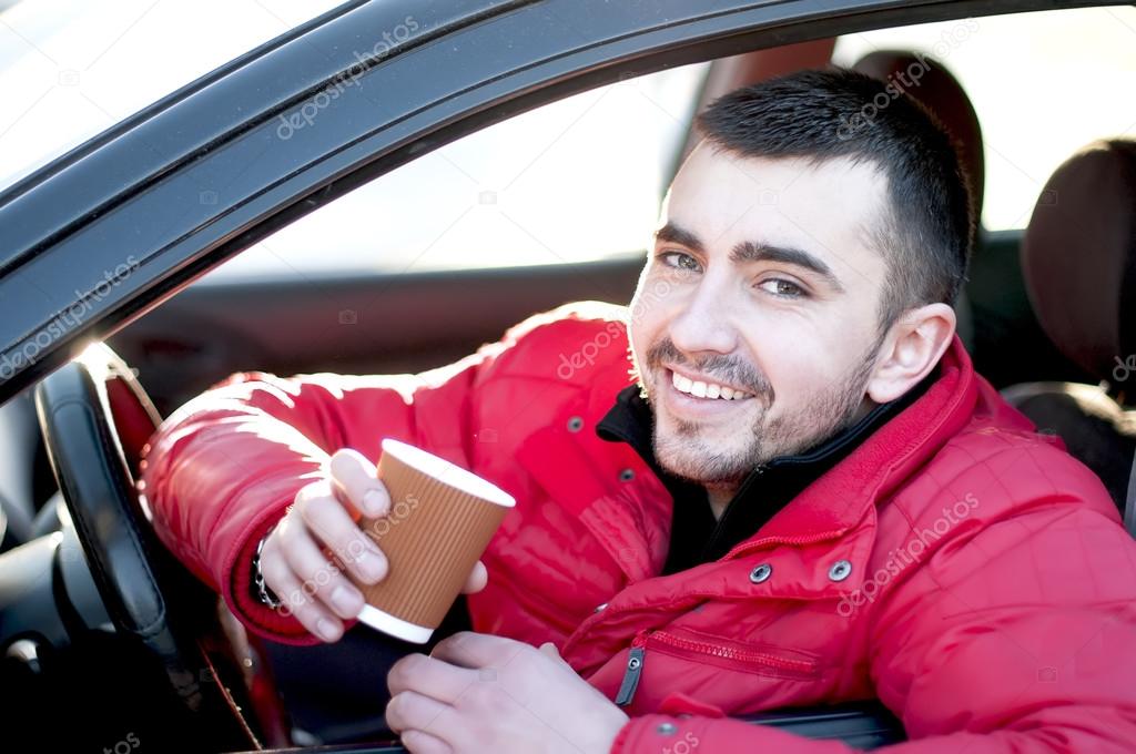 Attractive man in his  car drinking coffee outdoors.