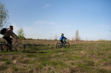 Baba ve küçük oğul çayırda bisiklete biniyorlar.