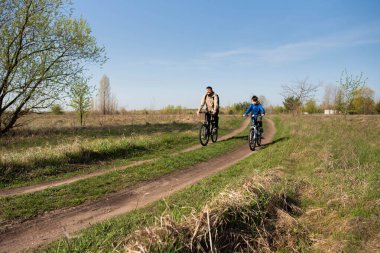 Baba ve küçük oğul çayırda bisiklete biniyorlar.