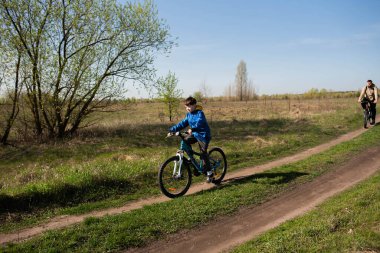 Baba ve küçük oğul çayırda bisiklete biniyorlar.