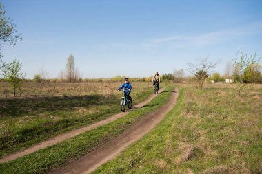Baba ve küçük oğul çayırda bisiklete biniyorlar.