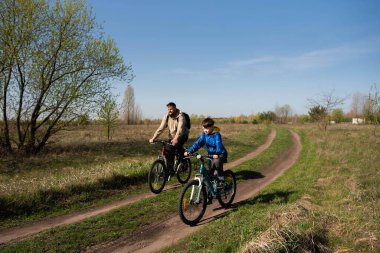 Baba ve küçük oğul çayırda bisiklete biniyorlar.