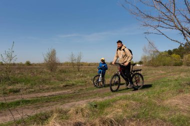 Baba ve küçük oğul çayırda bisiklete biniyorlar.