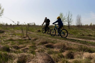 Baba ve küçük oğul çayırda bisiklete biniyorlar.