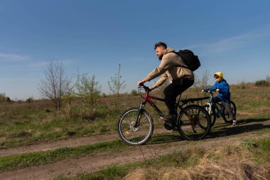 Baba ve küçük oğul çayırda bisiklete biniyorlar.