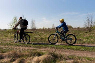 Baba ve küçük oğul çayırda bisiklete biniyorlar.