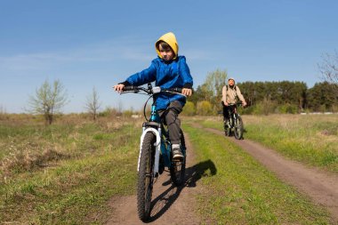 Baba ve küçük oğul çayırda bisiklete biniyorlar.