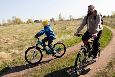 Baba ve küçük oğul çayırda bisiklete biniyorlar.