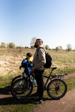 Baba ve küçük oğul çayırda bisiklete biniyorlar.