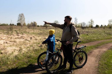 Baba ve küçük oğul çayırda bisiklete biniyorlar.