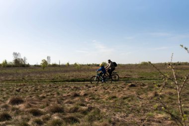 Baba ve küçük oğul çayırda bisiklete biniyorlar.
