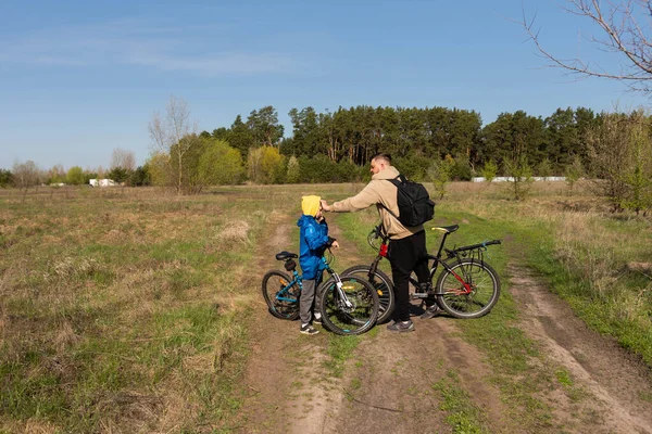 Baba ve küçük oğul çayırda bisiklete biniyorlar.