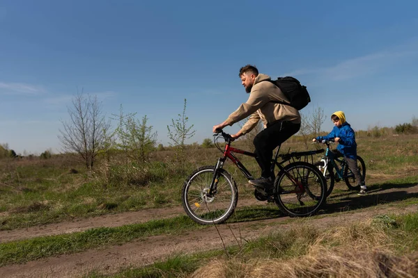 Baba ve küçük oğul çayırda bisiklete biniyorlar.