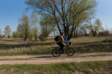 Babası küçük oğlunu bir çayırda bisikletin gidonuna bindiriyor.