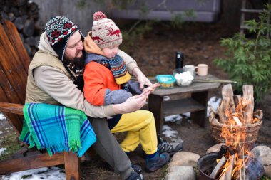 Baba oğul kışlık giysiler içinde ellerini ısıtıyorlar arka bahçede yanan bir ateşle.