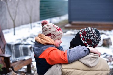 Oğlu ve babası kışın dışarıda otururken kucaklaşıp gülümsüyor.