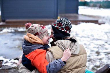 Oğlu ve babası kışın dışarıda otururken kucaklaşıp gülümsüyor.