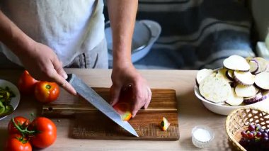 Sebze satay yapmak için tahta tahtada taze domates kesen bir adam.