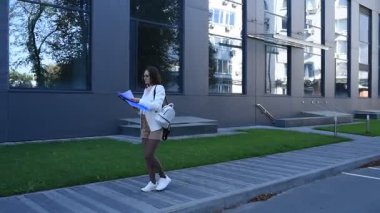 İş kadını işe giderken modern binanın önünden geçen belgelere göz atıyor.