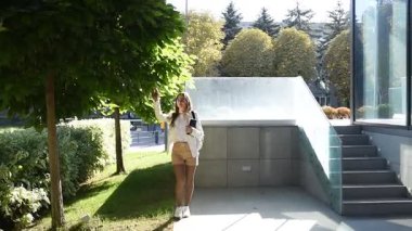 Katalpa ağaçlarının gölgesindeki modern bir şehir binasının terasında elinde defteriyle bir iş kadını.