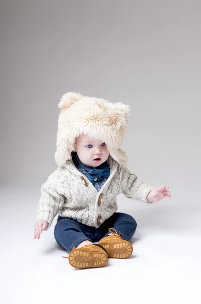 Legrační chlapeček v zimní srsti hat obal šedé pozadí. — Stock fotografie